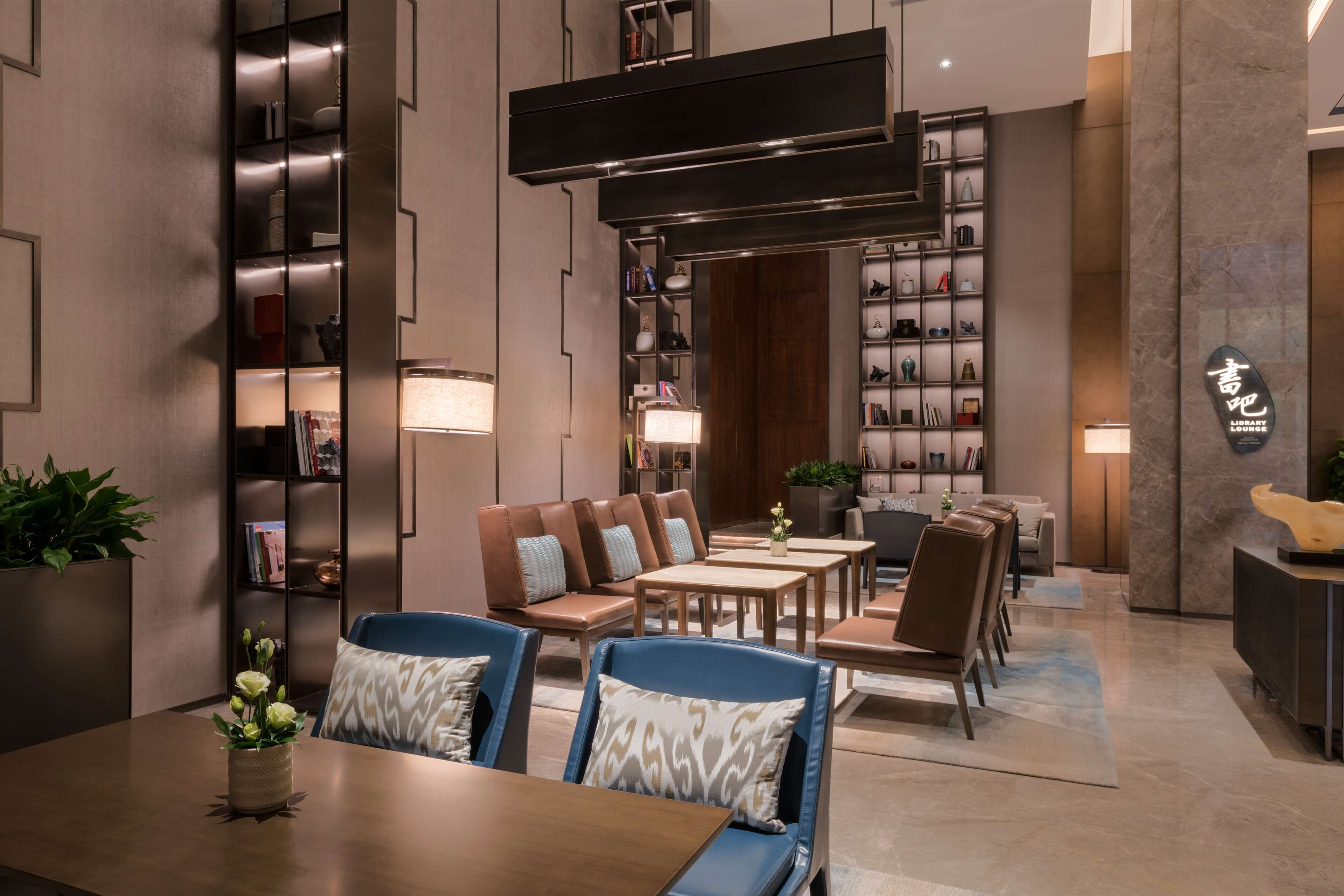 A modern hotel lobby with seating areas, bookshelves, and decorative lighting.