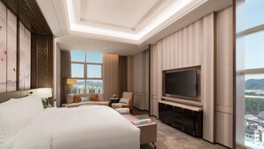 A modern hotel room with a large bed, a seating area, a flat-screen TV, and a city view. - DoubleTree by Hilton Hotel Shiyan (Shiyan)