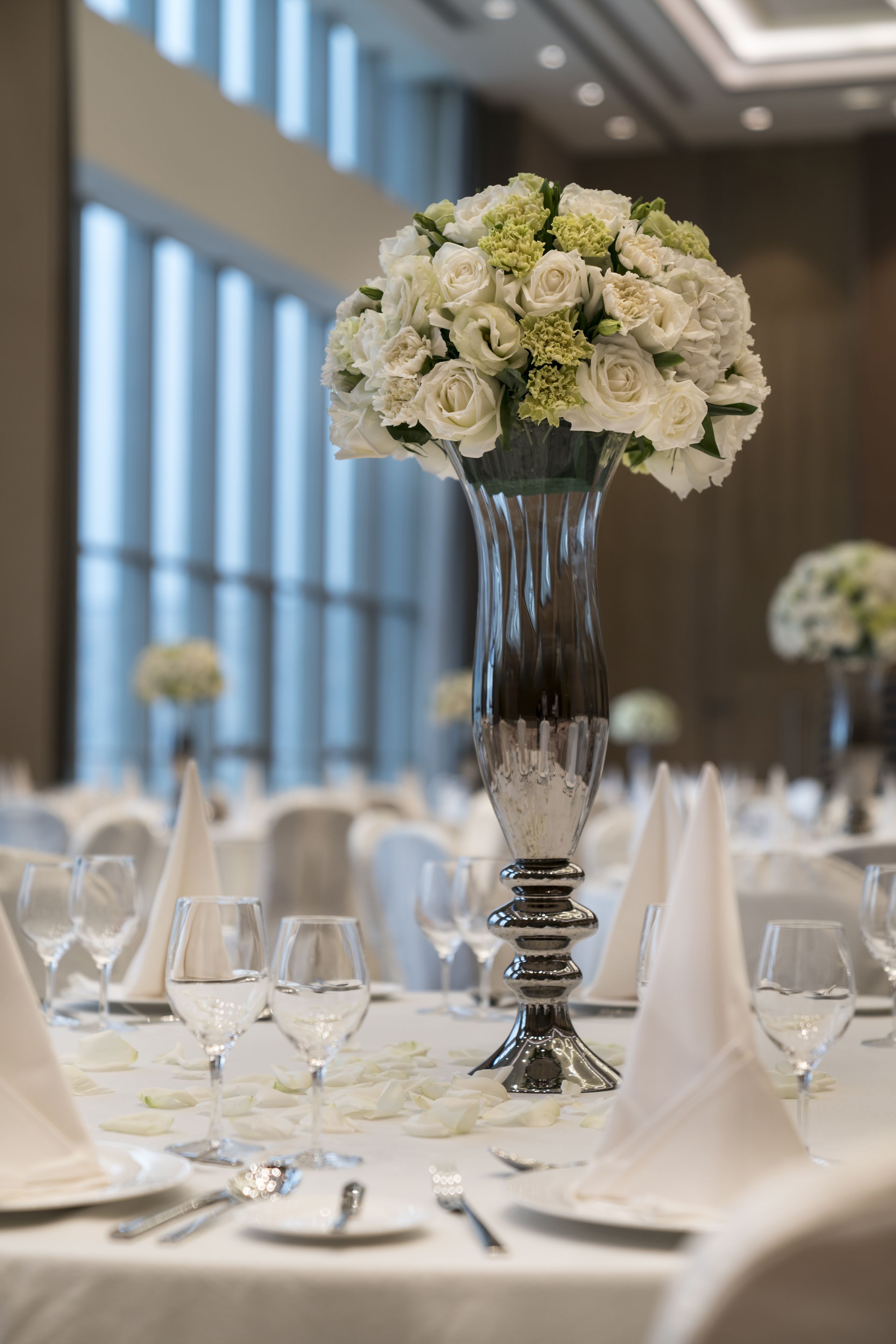 Una mesa dispuesta con manteles blancos, cubiertos de plata y un jarrón de flores blancas.