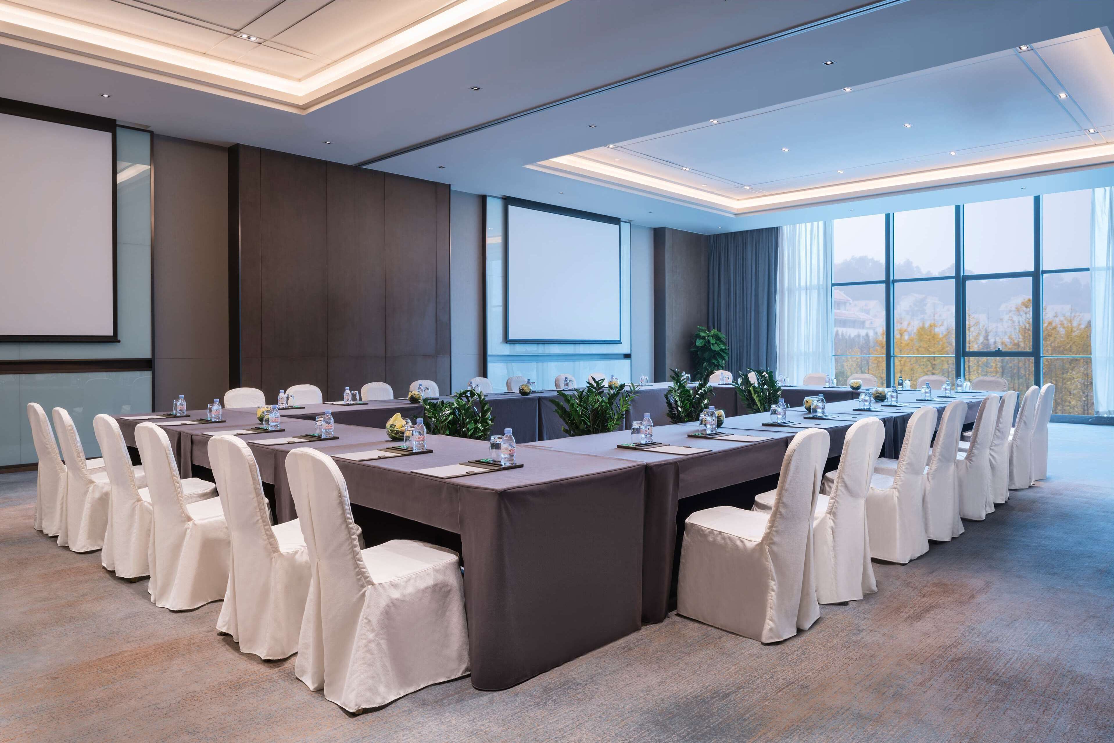 Una sala de conferencias con una mesa larga, sillas blancas y un ventanal con vistas.