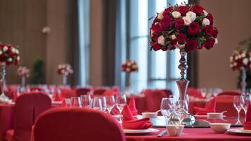 Ein Festsaal mit gedeckten Tischen für eine festliche Veranstaltung, mit roten Tischdecken und floralen Mittelpunkten.