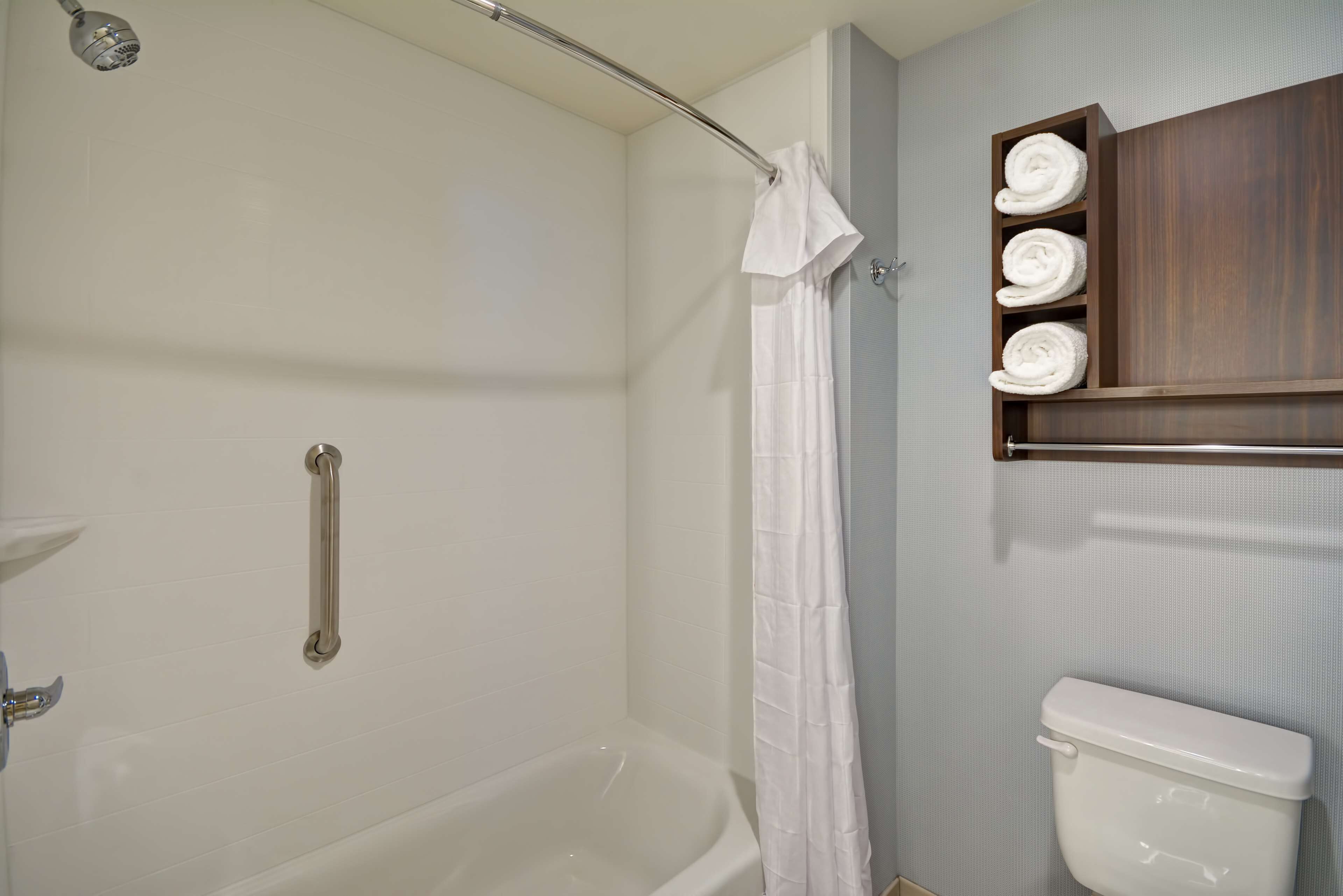 A bathroom with a bathtub, a toilet, a shower curtain, a towel rack with towels, and a handrail.