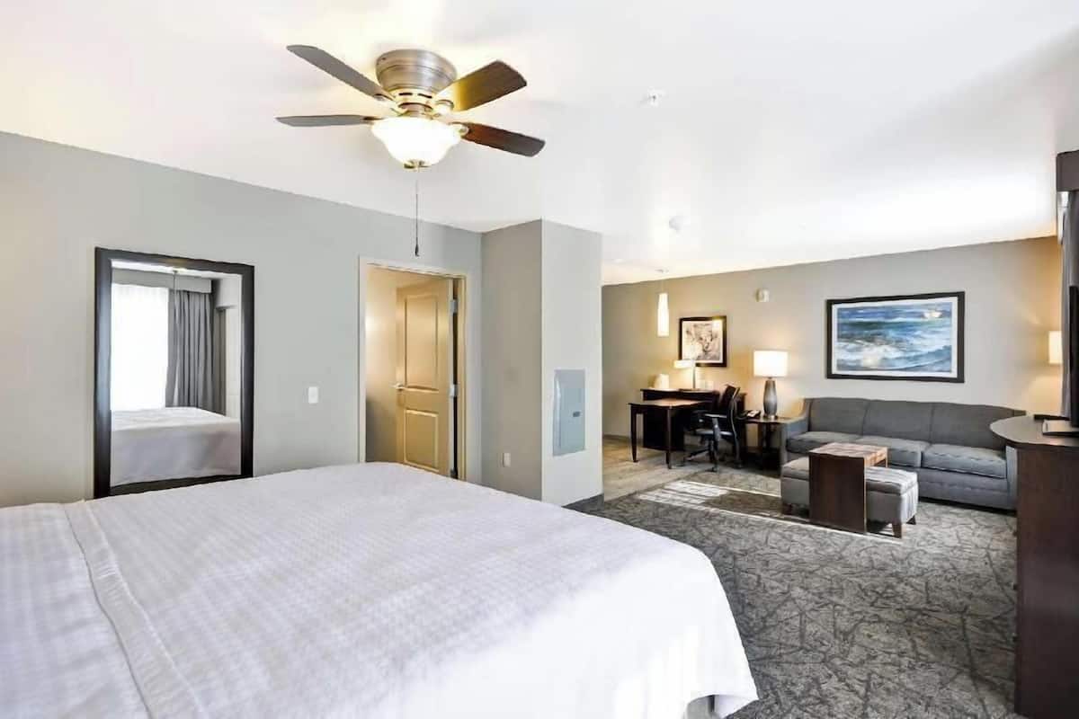 A hotel room with a bed, a desk, a sofa, a ceiling fan, and a painting on the wall.
