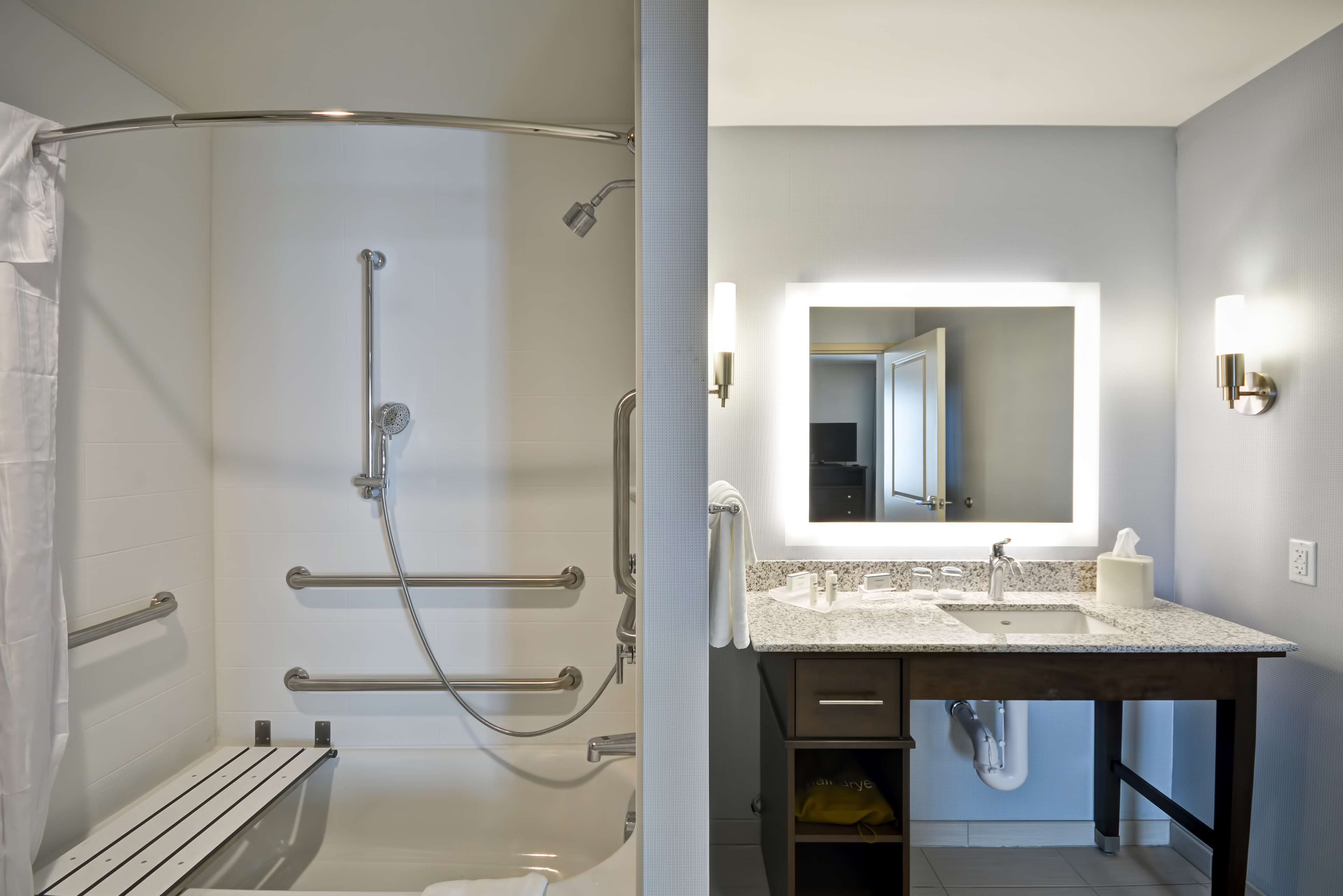 A modern bathroom with a walk-in shower, grab bars, a vanity with a sink, and a mirror.