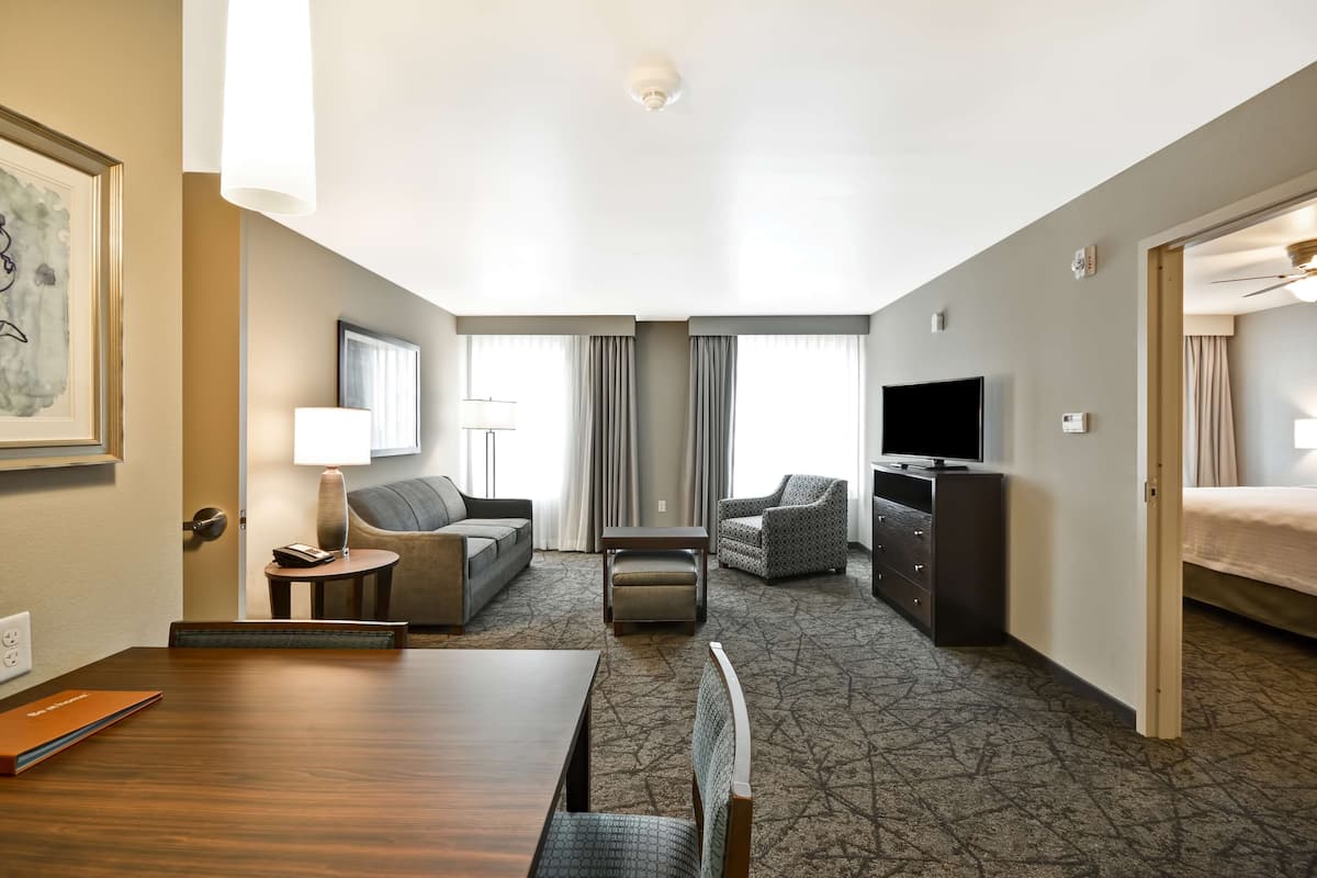 A hotel room with a dining table, sofa, armchair, TV, and a bed.