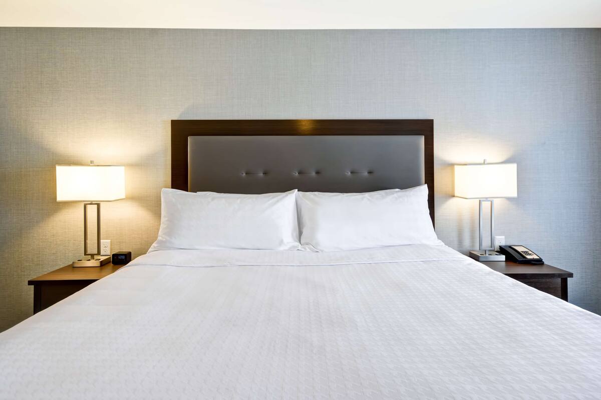 A neatly made bed with a wooden headboard, two bedside tables with lamps, and a phone on one of the tables.