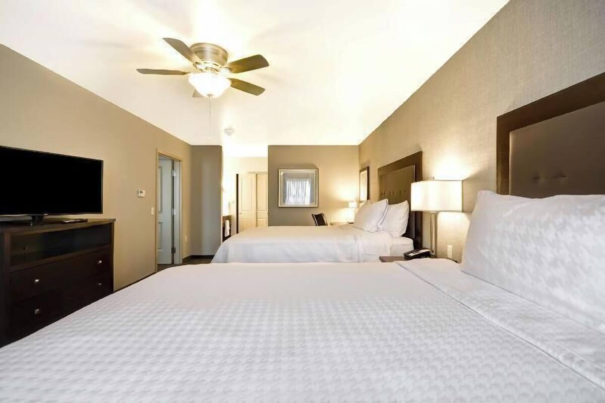A hotel room with two beds, a ceiling fan, a flat-screen TV, and a bedside lamp.