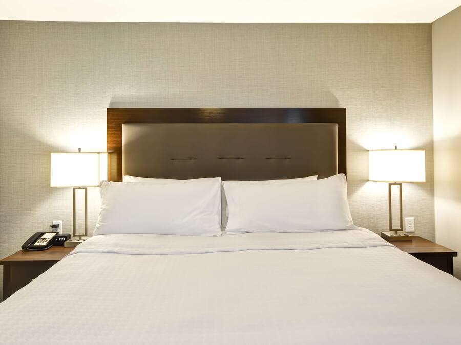 A neatly made bed with white linens, two bedside lamps, a phone on the left nightstand, and a small table with a lamp on the right.
