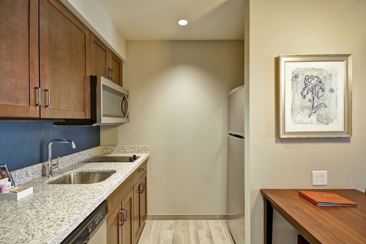 A kitchen with granite countertops, stainless steel sink, wooden cabinets, a microwave, and a refrigerator.