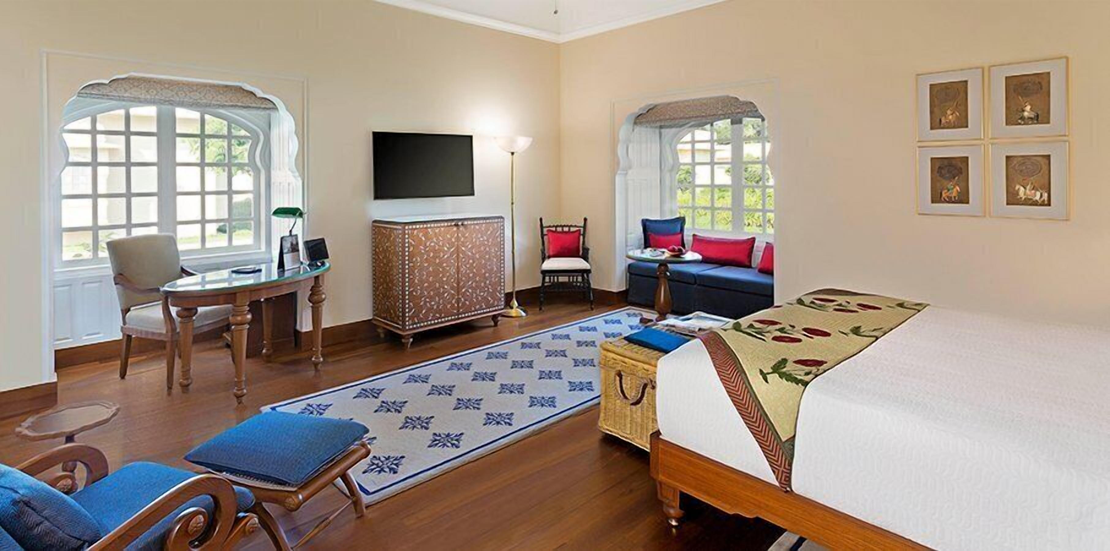 A hotel room with a bed, a desk, a chair, a television, and a window with a view of greenery.
