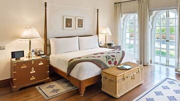 A four-poster bed with a wooden frame, two bedside tables with lamps, a wicker side table, and a view of the outdoors through large arched windows.