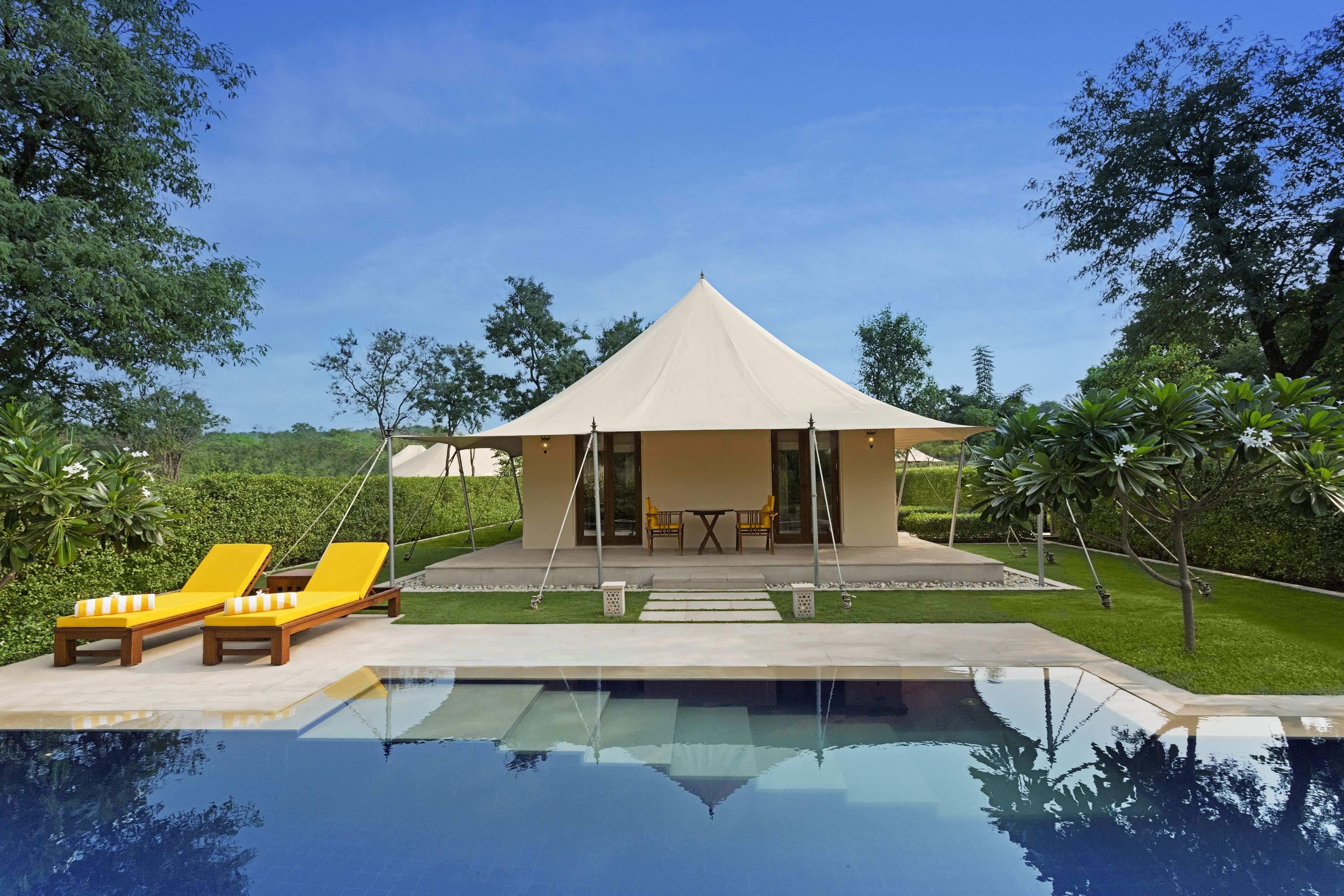 Una villa moderna con piscina, sillas de descanso amarillas y un porche cubierto.