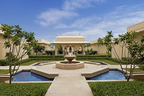 A courtyard with a central fountain, surrounded by pools and palm trees, leading to a building with a dome. - The Oberoi Sukhvilas Spa Resort, New Chandigarh (Kharar)