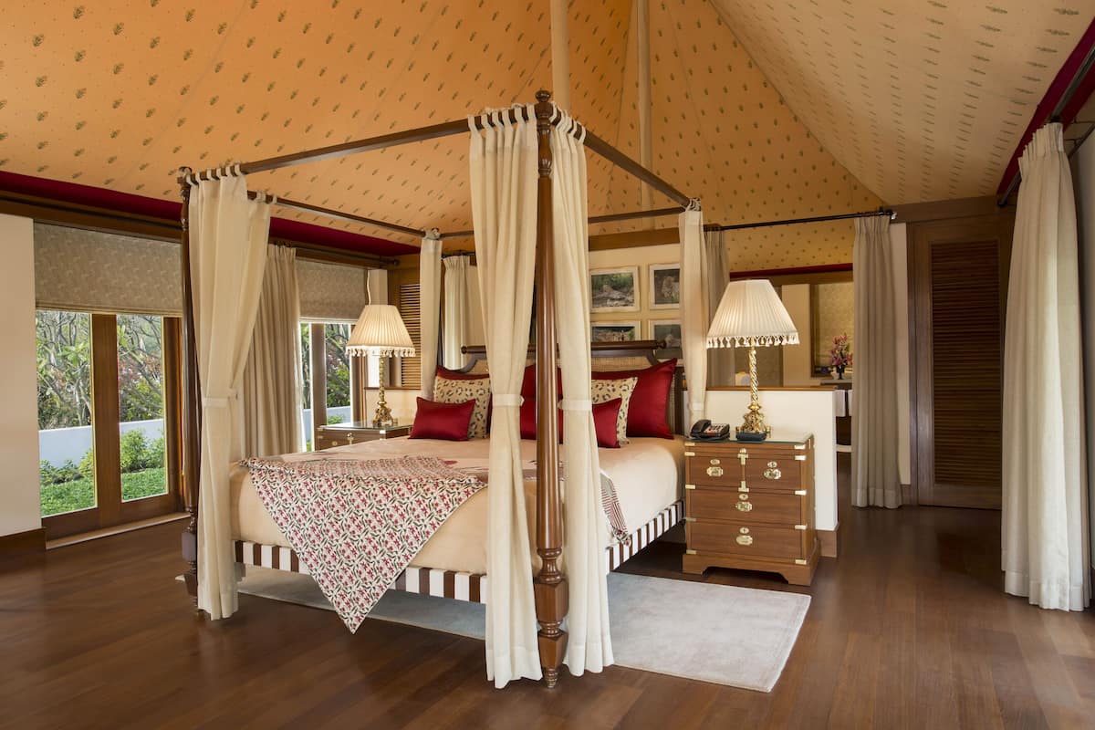 A four-poster canopy bed with a wooden frame, a bedside table with a lamp, and a nightstand with a phone.