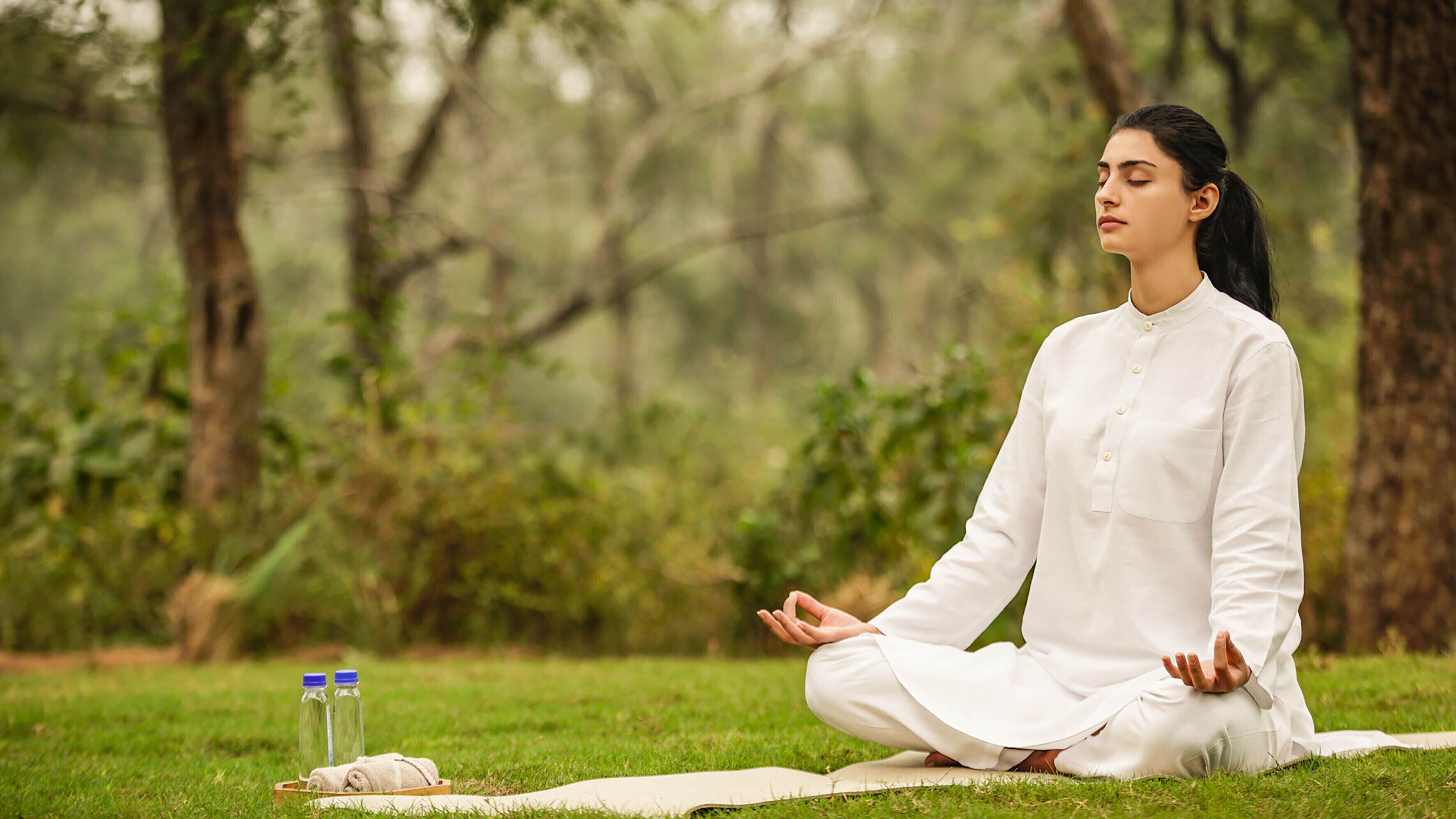 A person meditating in a park with trees and grass.