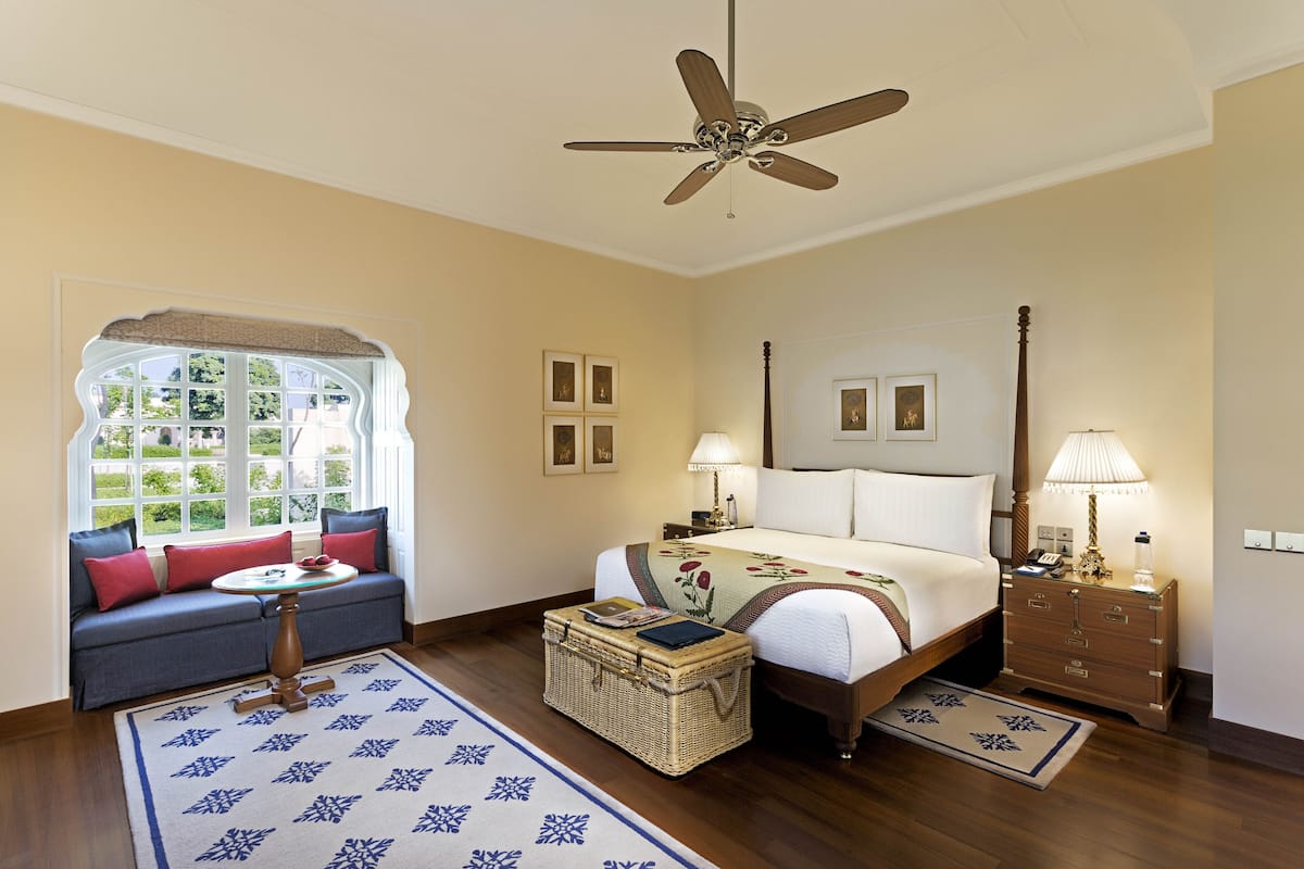 A bedroom with a bed, nightstand, lamp, dresser, window, and a sofa with a table.