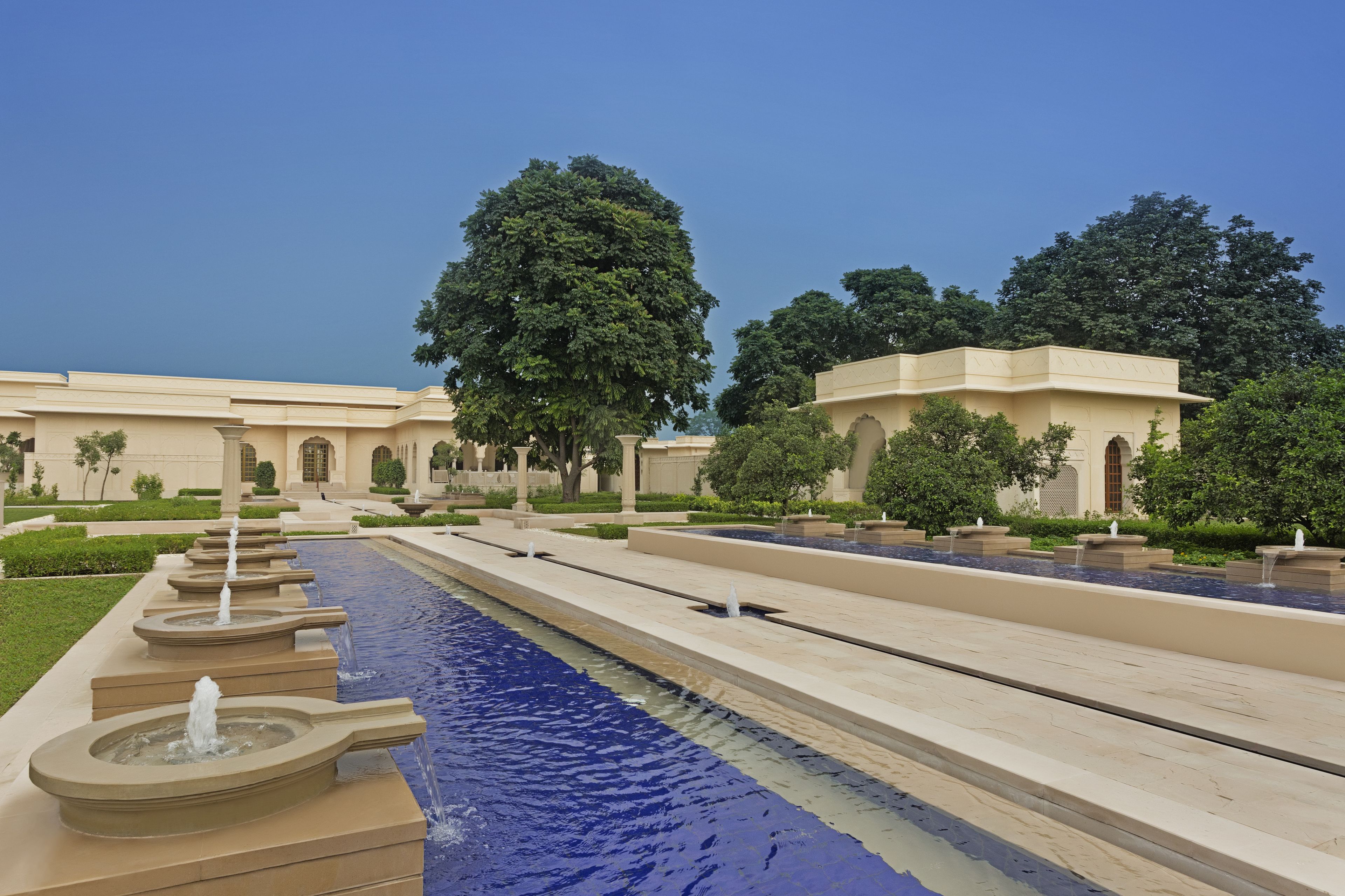 Una larga y estrecha fuente con múltiples fuentes, rodeada de jardines cuidados y arquitectura clásica.