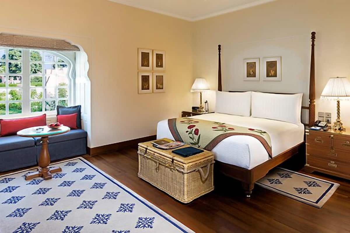 A bedroom with a bed, a sofa, a nightstand, a lamp, a dresser, and a window with a view.