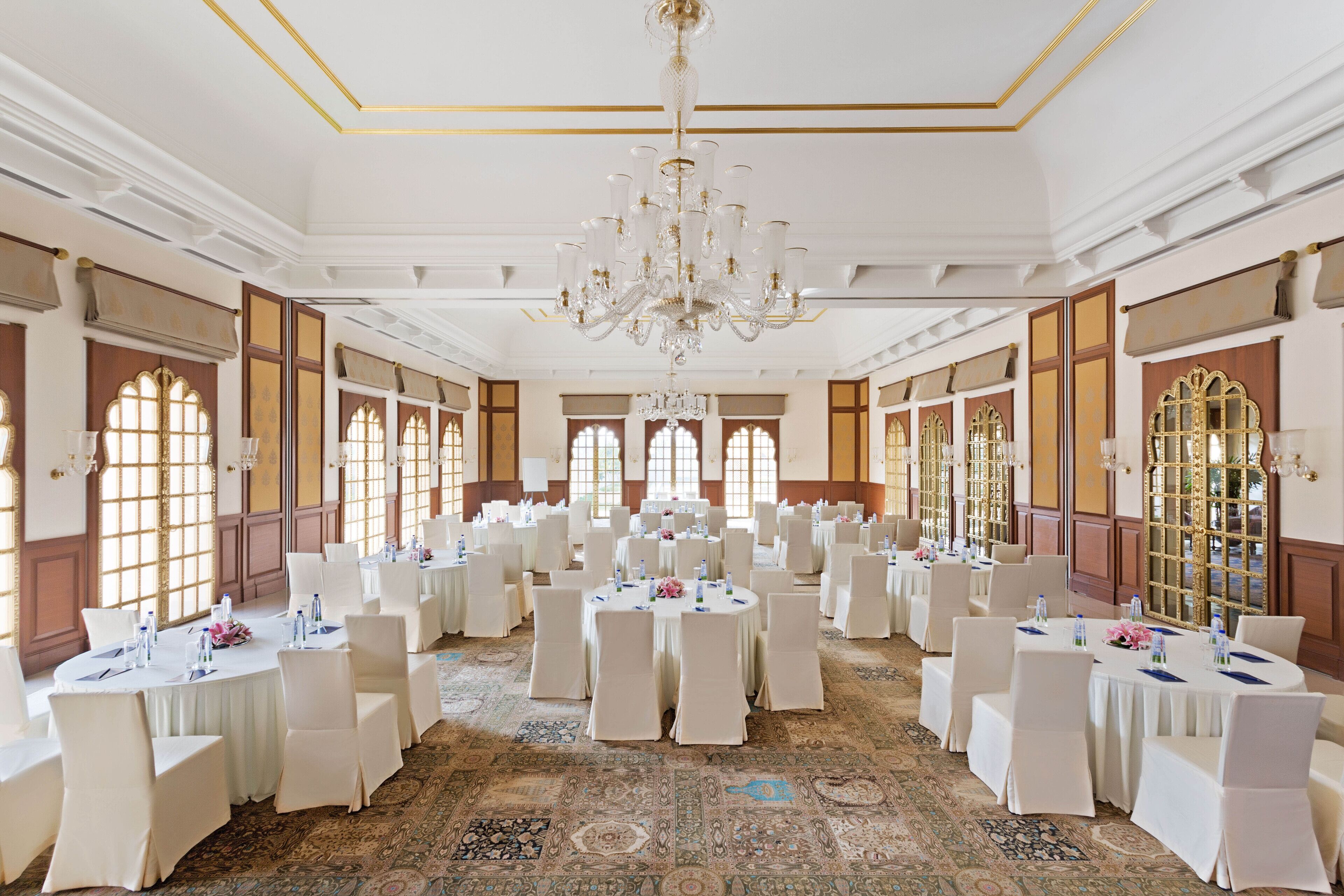 A banquet hall with round tables, white chairs, and chandeliers.