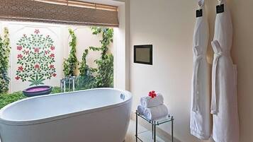 Un baño con una bañera independiente, un perchero de vidrio con toallas y un cuadro enmarcado en la pared.