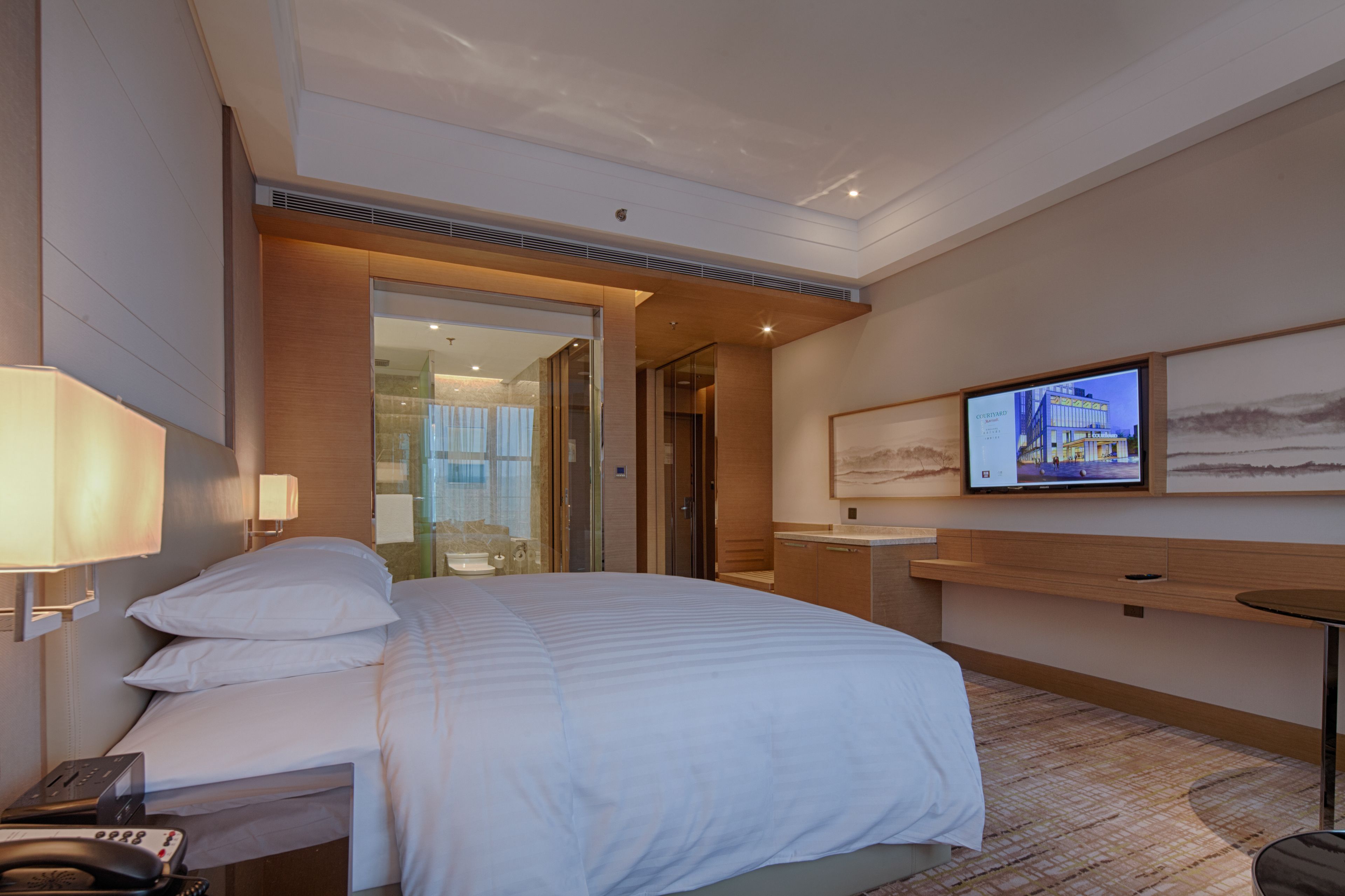 A hotel room with a large bed, a bedside table, a TV mounted on the wall, and a bathroom visible through an open door.