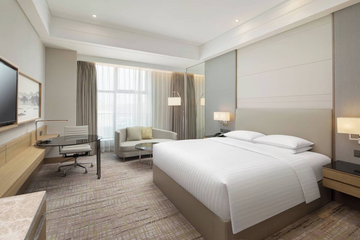 A hotel room with a large bed, a desk with a chair, a sofa, and a TV on the wall.