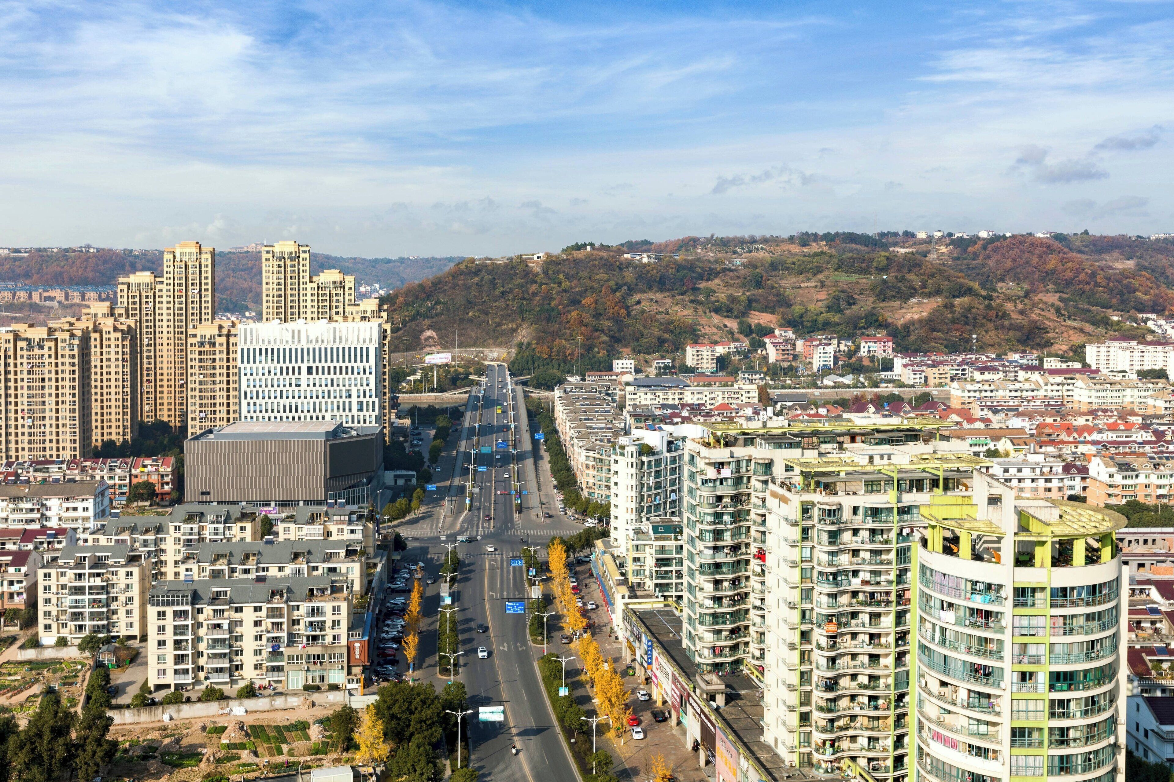 Un paisaje urbano con rascacielos, una avenida principal y un fondo montañoso.