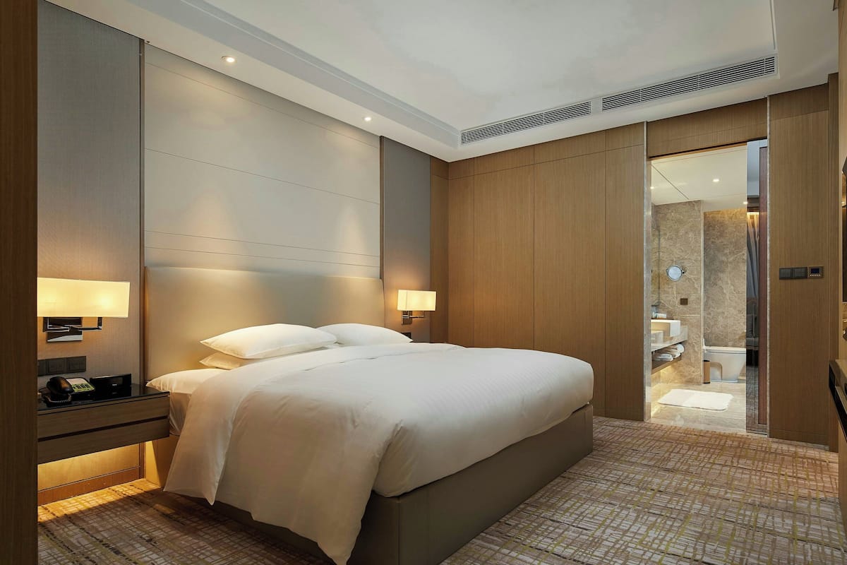 A modern hotel room with a large bed, bedside lamps, a nightstand, and a view into the bathroom.