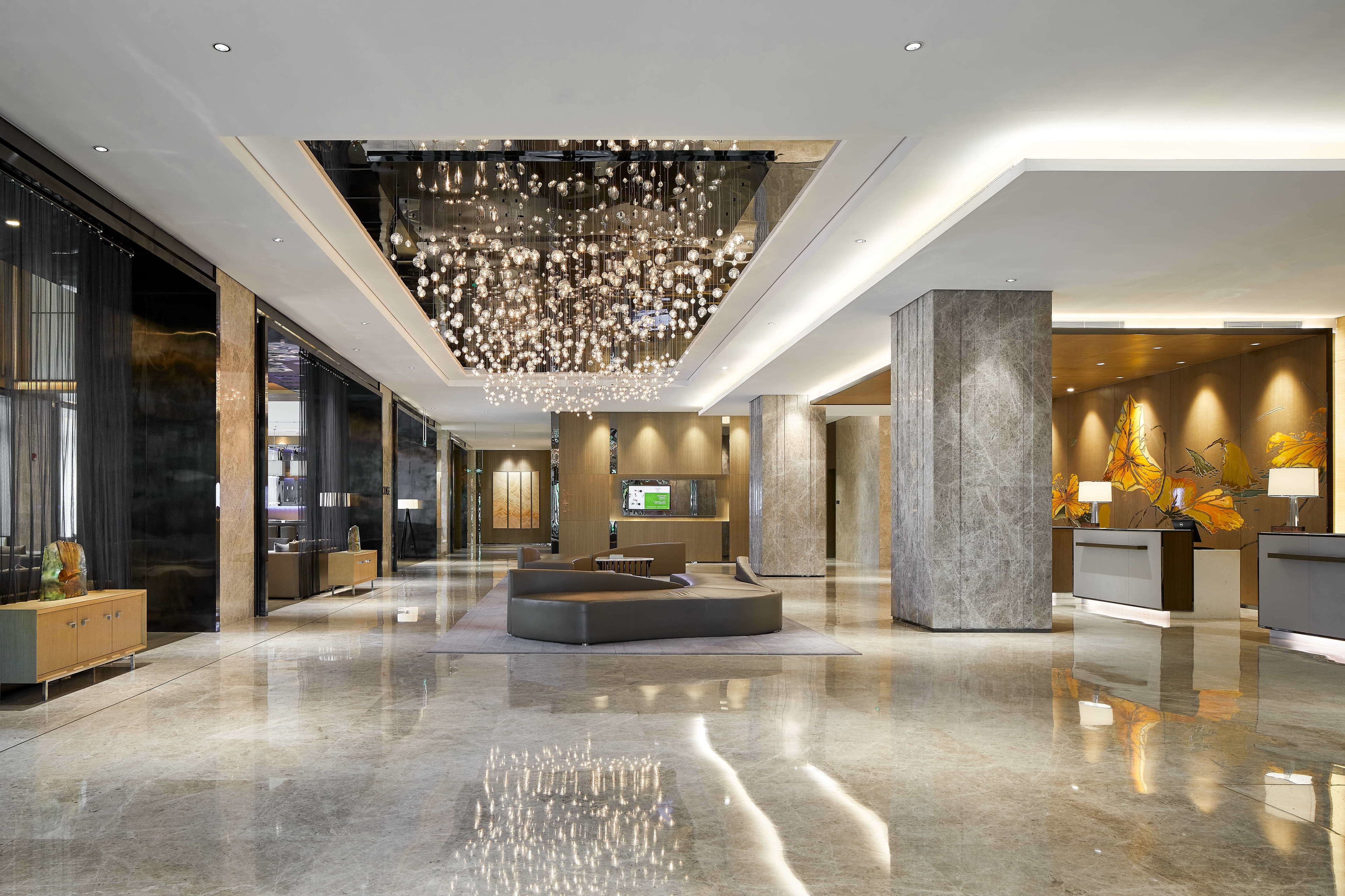 A spacious lobby with a reflective floor, a central seating area, and a large chandelier.