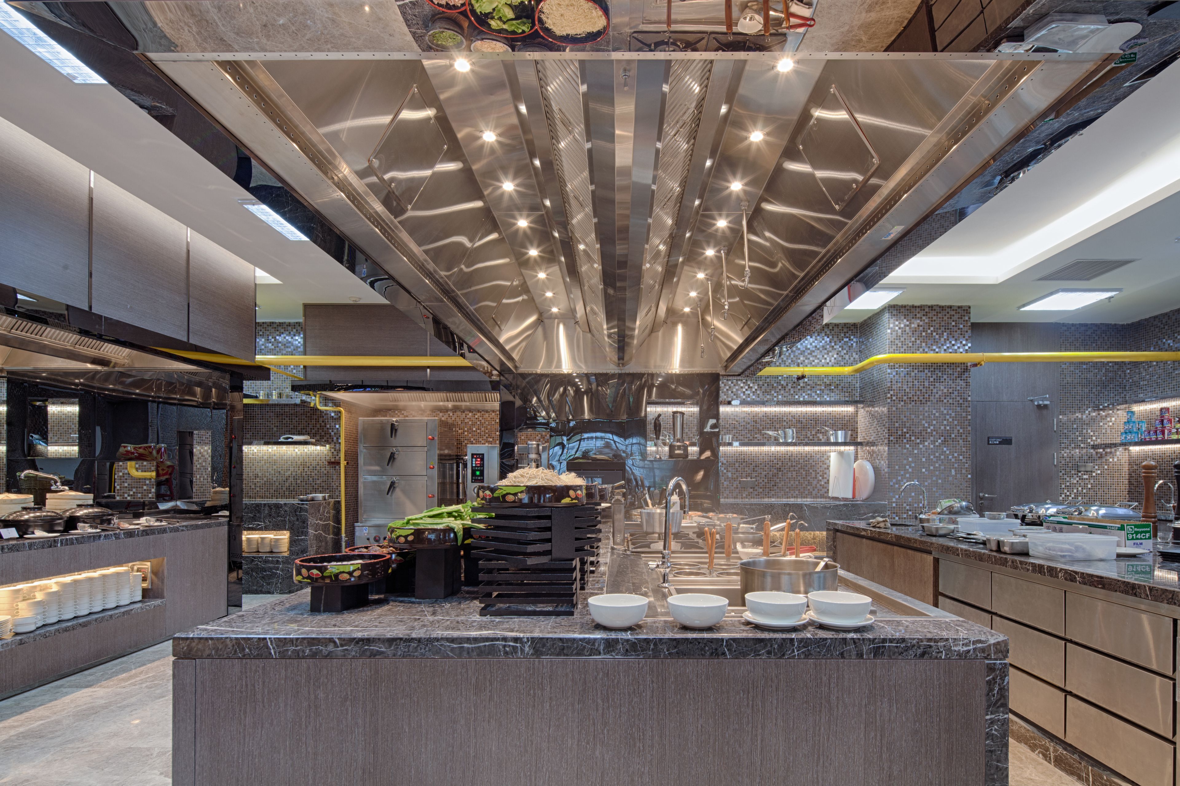 A modern kitchen with a central island, stainless steel appliances, and a high ceiling with linear lighting.