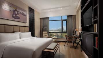 A hotel room with a large bed, a desk with a chair, a television, and a bookshelf.
