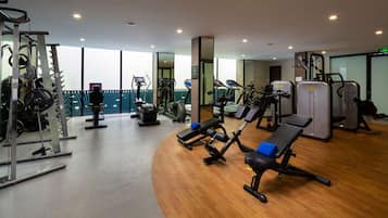 Une salle de sport moderne équipée de divers appareils d’exercice, dotée de grandes fenêtres et d’un plancher en bois.