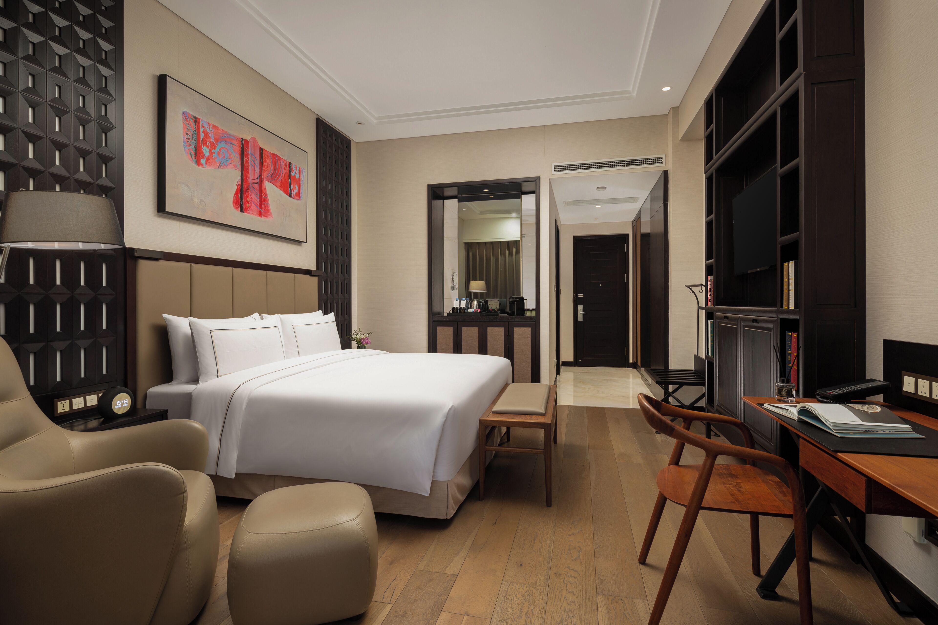 A hotel room with a bed, a desk, a chair, a TV, and a bookshelf.