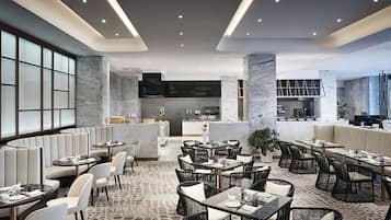 Un restaurante moderno con mesas redondas y cabinas, columnas de mármol y una alfombra estampada.
