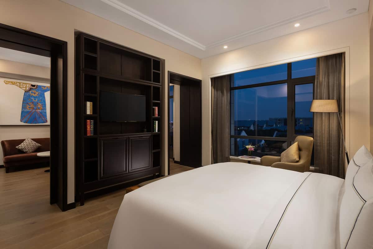 A hotel room with a large bed, a TV, a bookshelf, a sofa, and a view of the city at night.
