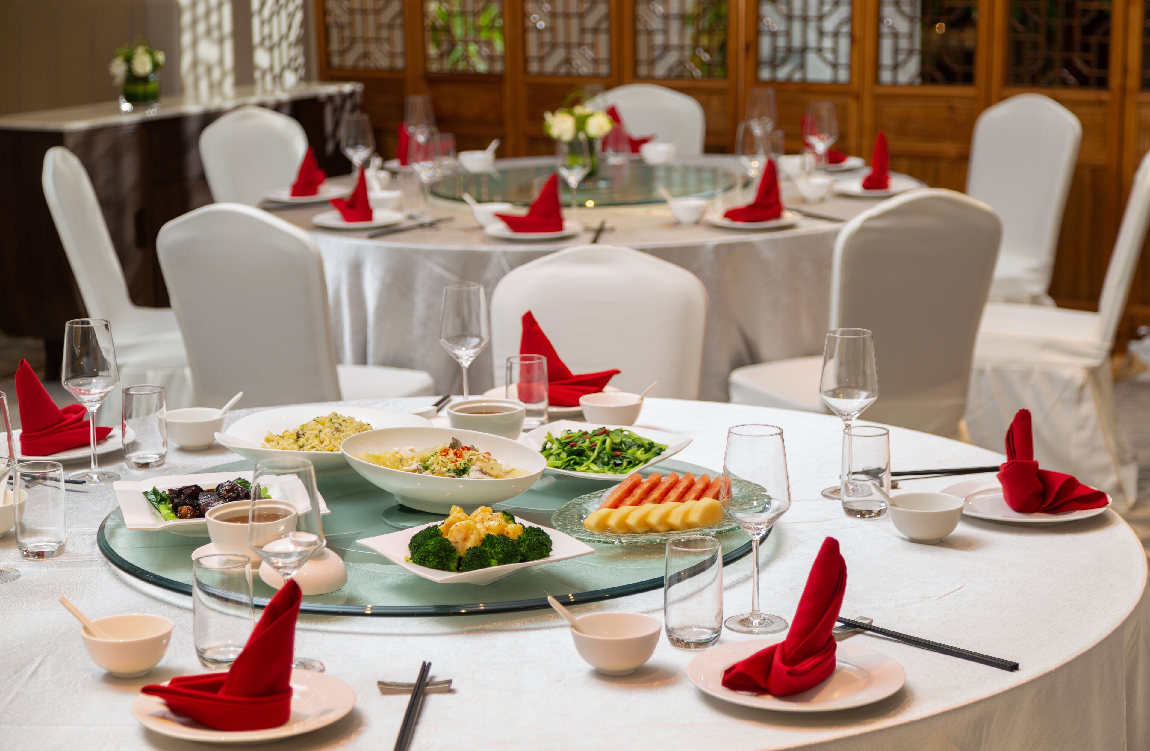 A formal dining setup with multiple tables, white chairs, and red napkins.