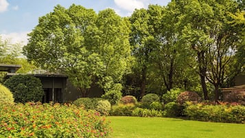 Ein gepflegter Garten mit verschiedenen Pflanzen und einem Rasen, ein Gebäude mit einem geneigten Dach und einem klaren Himmel.