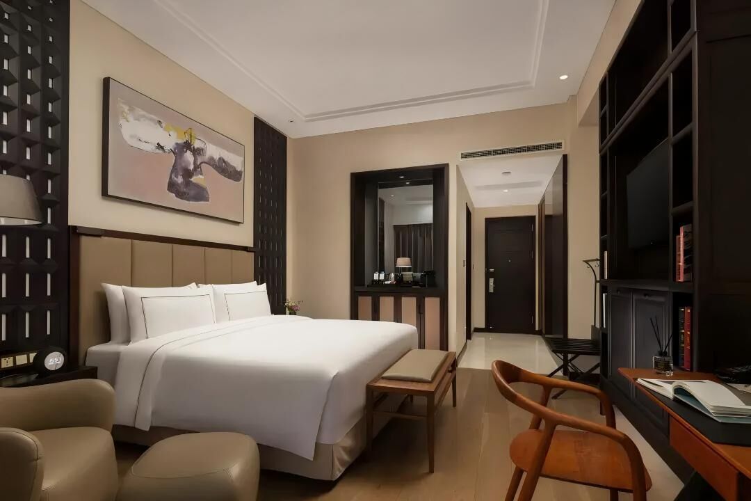 Een hotelkamer met een bed, een bureau, een stoel, een boekenkast en een schilderij aan de muur.