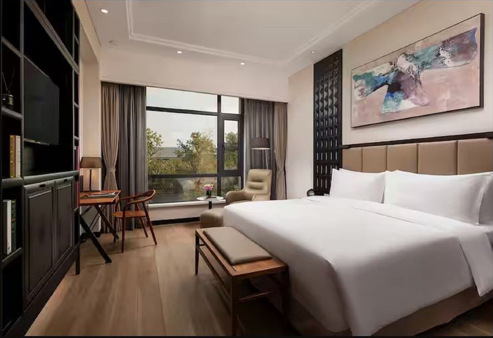 A hotel room with a large bed, a desk, a chair, a TV, and a window with a view.