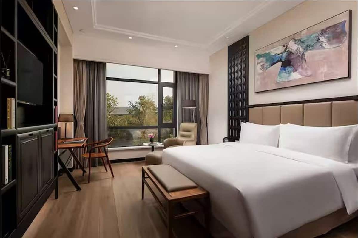 A hotel room with a large bed, a desk, a chair, a TV, and a window with a view.
