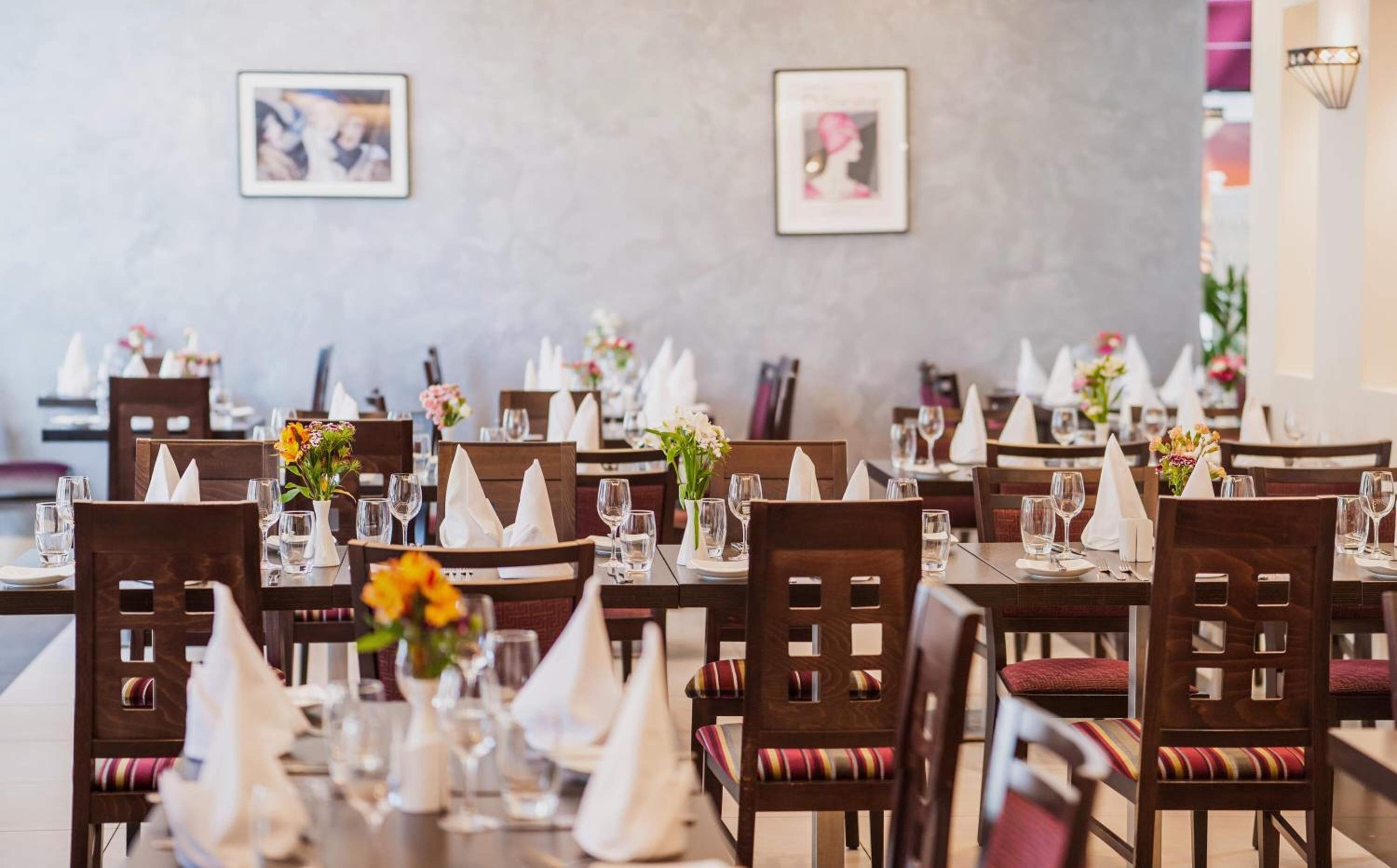 A restaurant with wooden chairs, white tablecloths, and floral centerpieces.