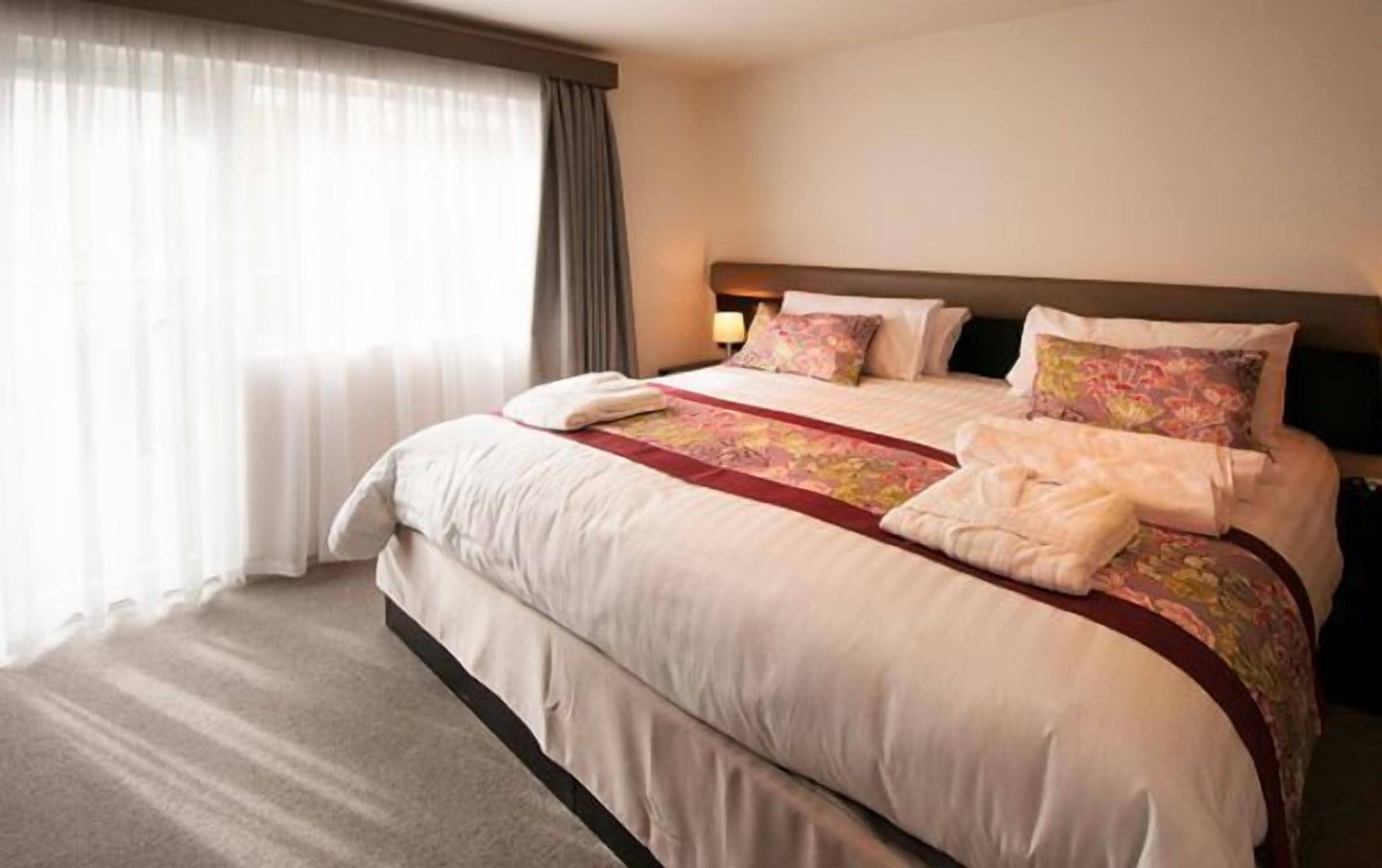 A hotel room with a large bed, a bedside table with a lamp, and a window with curtains.