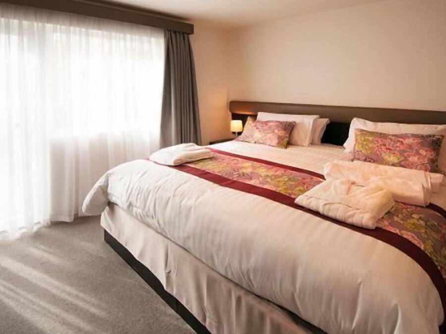 A hotel room with a large bed, a bedside table with a lamp, and a window with curtains.