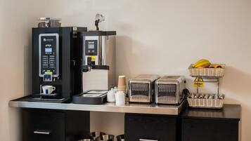 Una estación de café con una cafetera, un tostador y cestas de plátanos y naranjas.