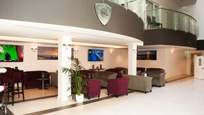 Um lobby moderno com áreas de estar, um relógio grande e várias telas exibindo conteúdo.