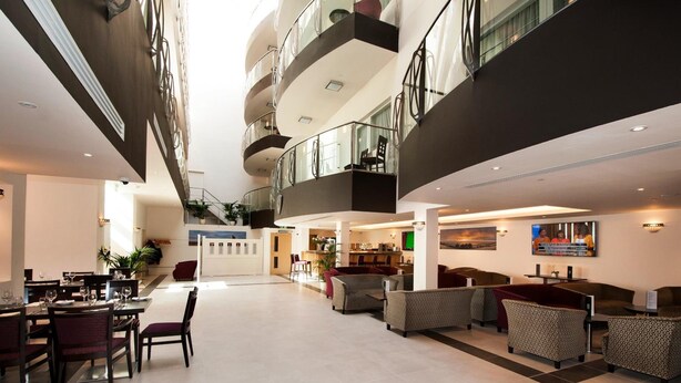 Um hall de hotel espaçoso com área de estar central, um bar e uma escadaria que dá acesso aos andares superiores.