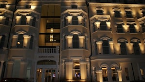 Um edifício histórico com vários andares, apresentando detalhes arquitetônicos clássicos como janelas em arco e molduras decorativas. O edifício está iluminado à noite, realçando sua fachada ornamentada.