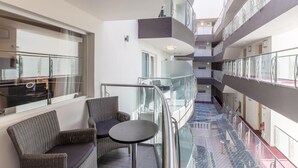 Interior moderno de hotel com guarda-corpo de vidro, mobiliário de vime e um átrio central.