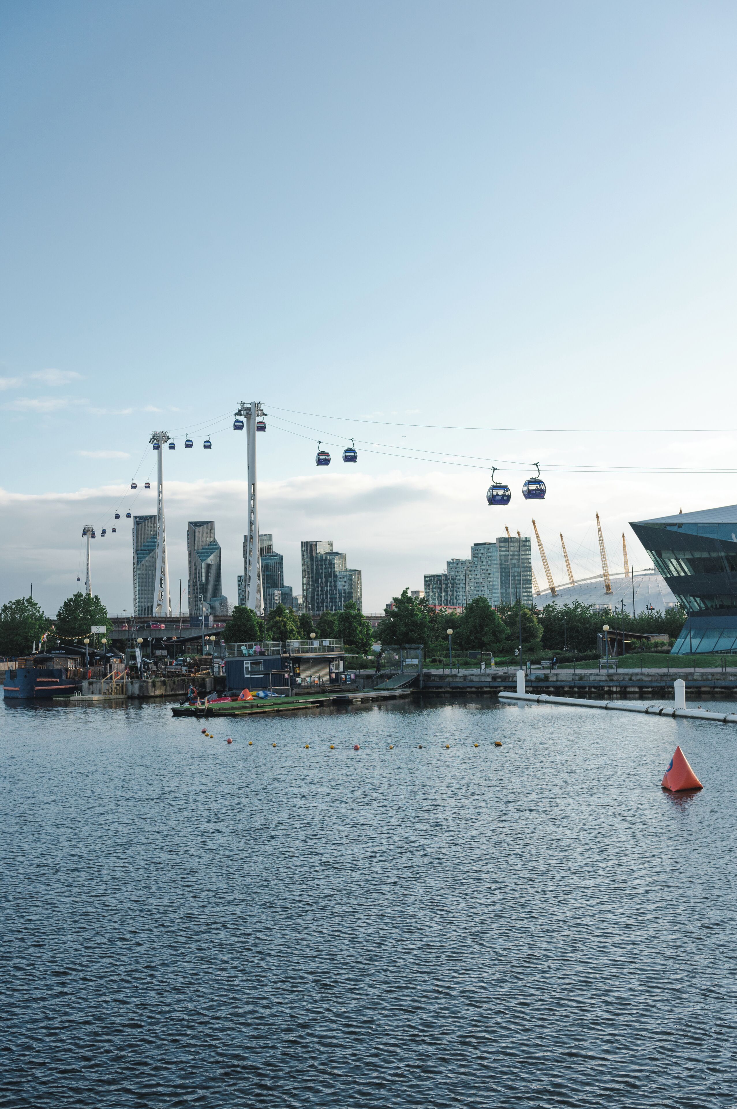 A waterfront cityscape with modern buildings, a marina, and a cable car system.