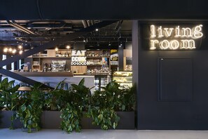 Uma área de bar moderna com um letreiro de neon que diz 'sala de estar' e o slogan 'coma, beba, faça o bem'.